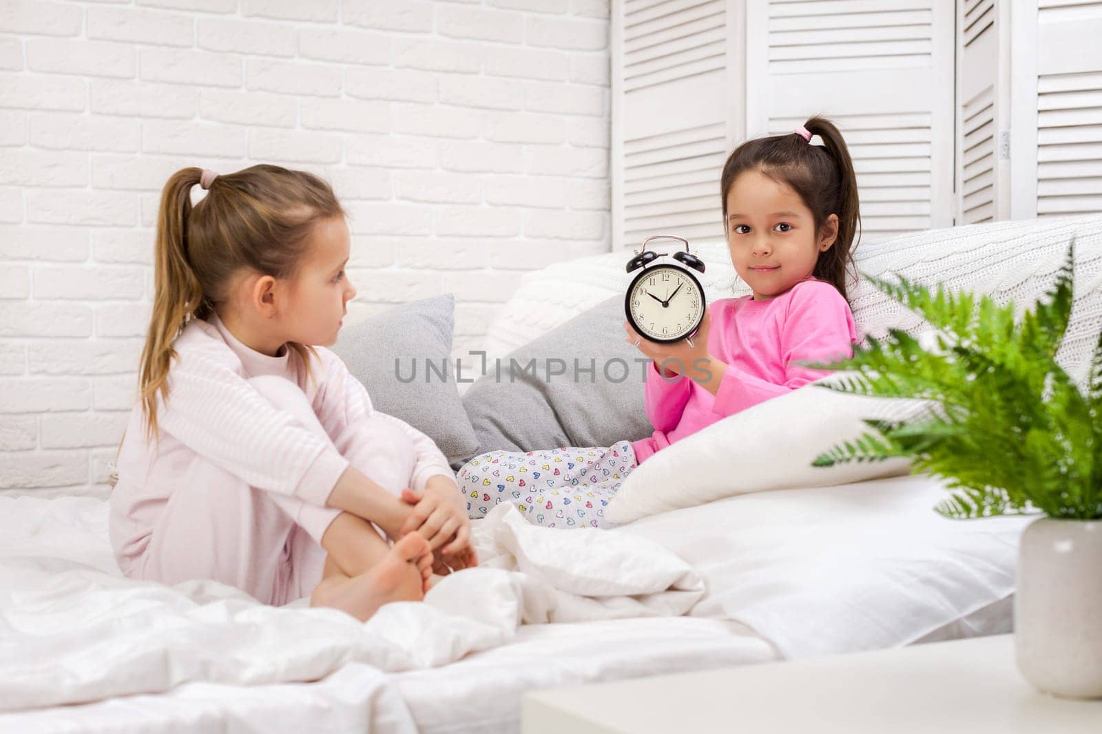 two cute children girls with clock in bed in the morning