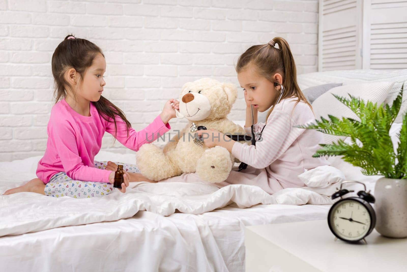 two cute children girls playing doctor with teddy bear at home. girl listens a stethoscope to toy.