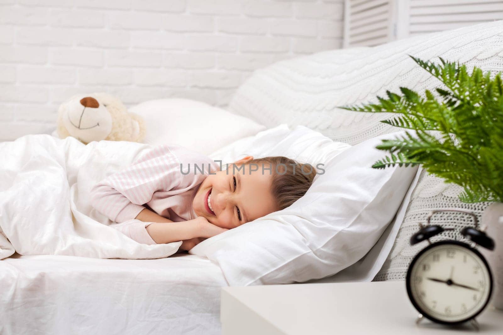 smiling little child girl sleeping with teddy bear in her bed