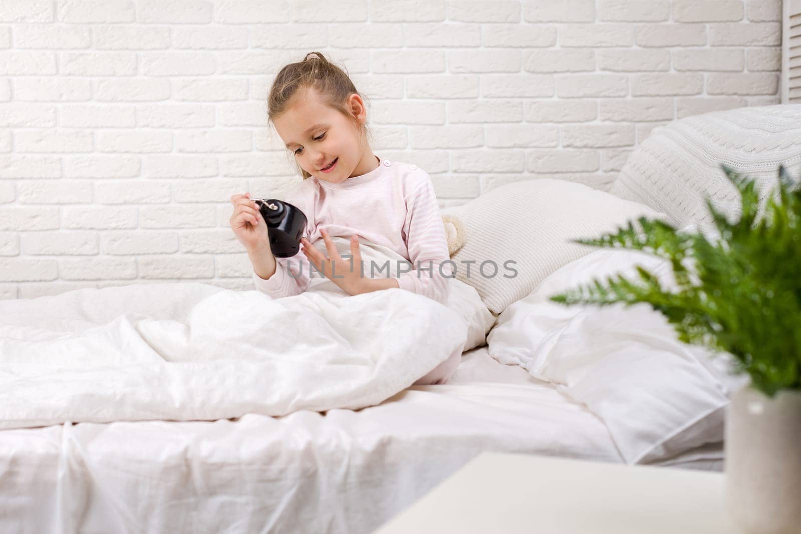cute little child girl in pyjamas with clock in bed. good morning