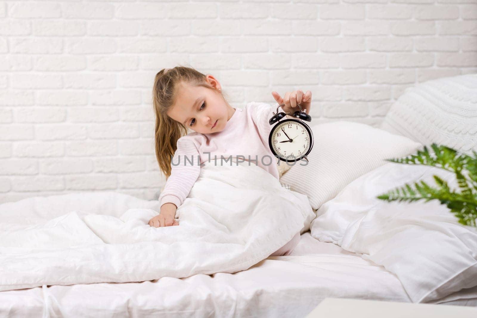 cute little child girl in pyjamas with clock in bed. good morning