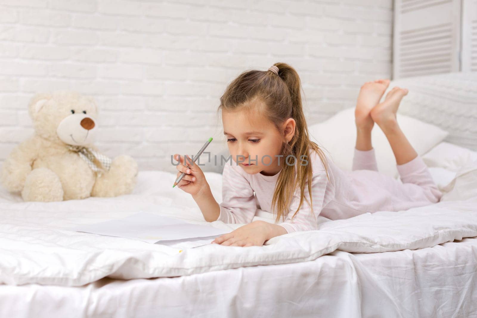 cute little girl drawing pictures while lying on bed. Kid painting at home