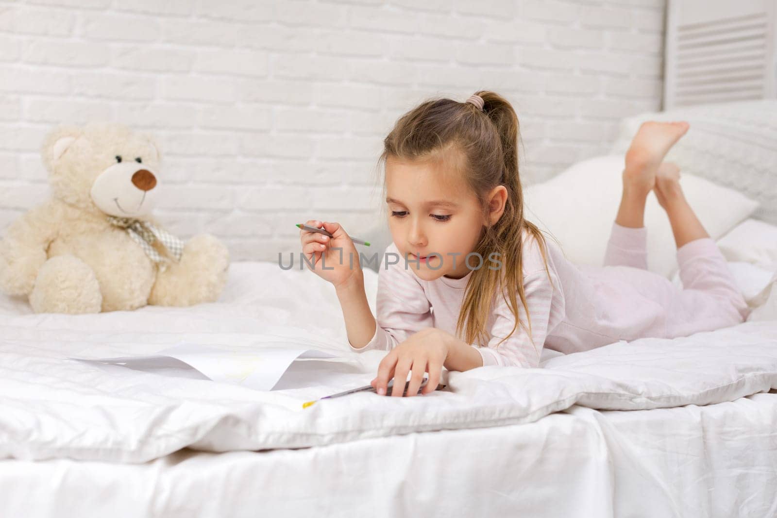 cute little girl drawing pictures while lying on bed. Kid painting at home