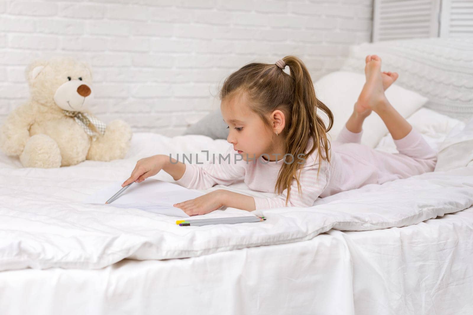 cute little girl drawing pictures while lying on bed. Kid painting at home