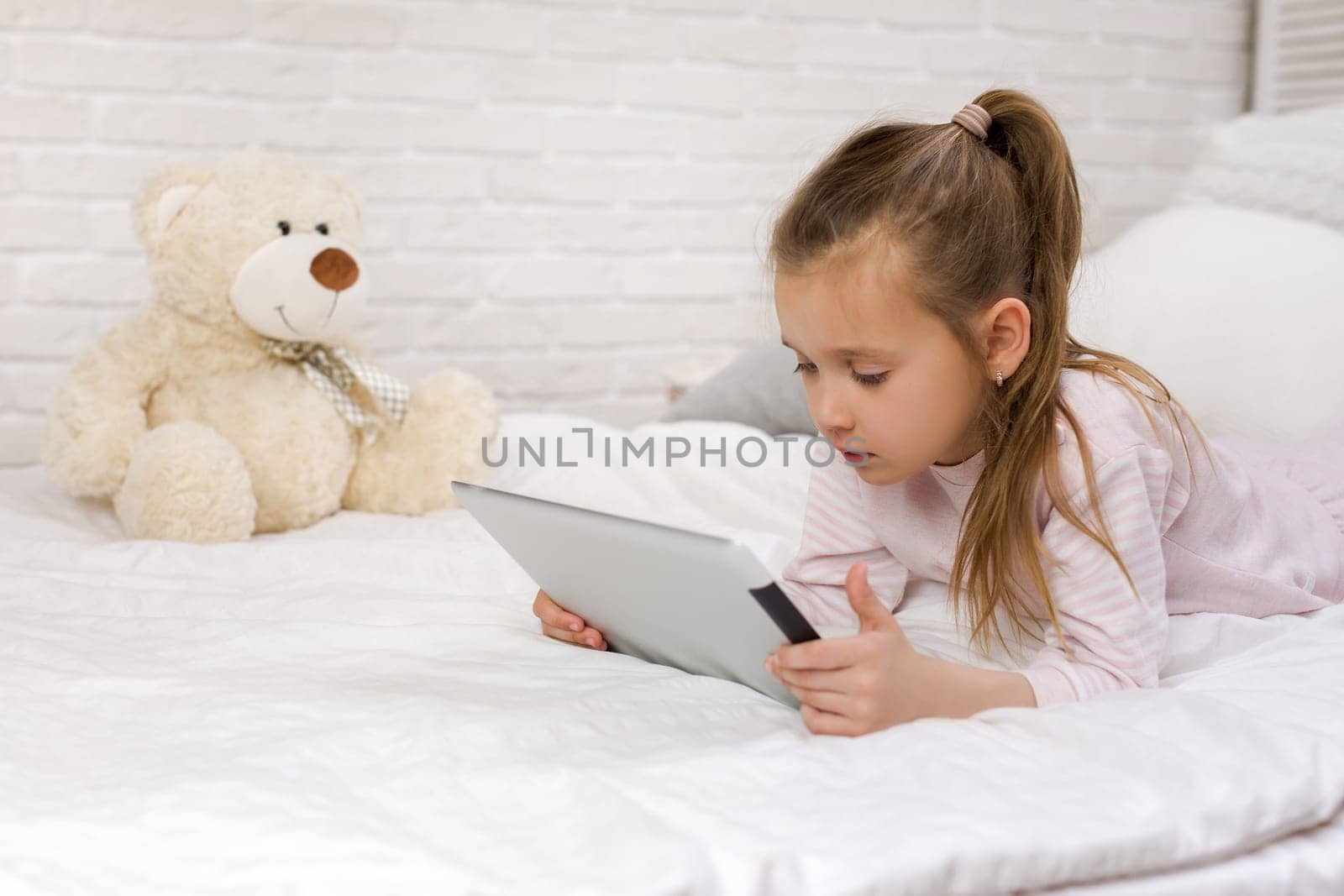 cute little child girl lies in bed uses digital tablet. child playing on tablet pc.