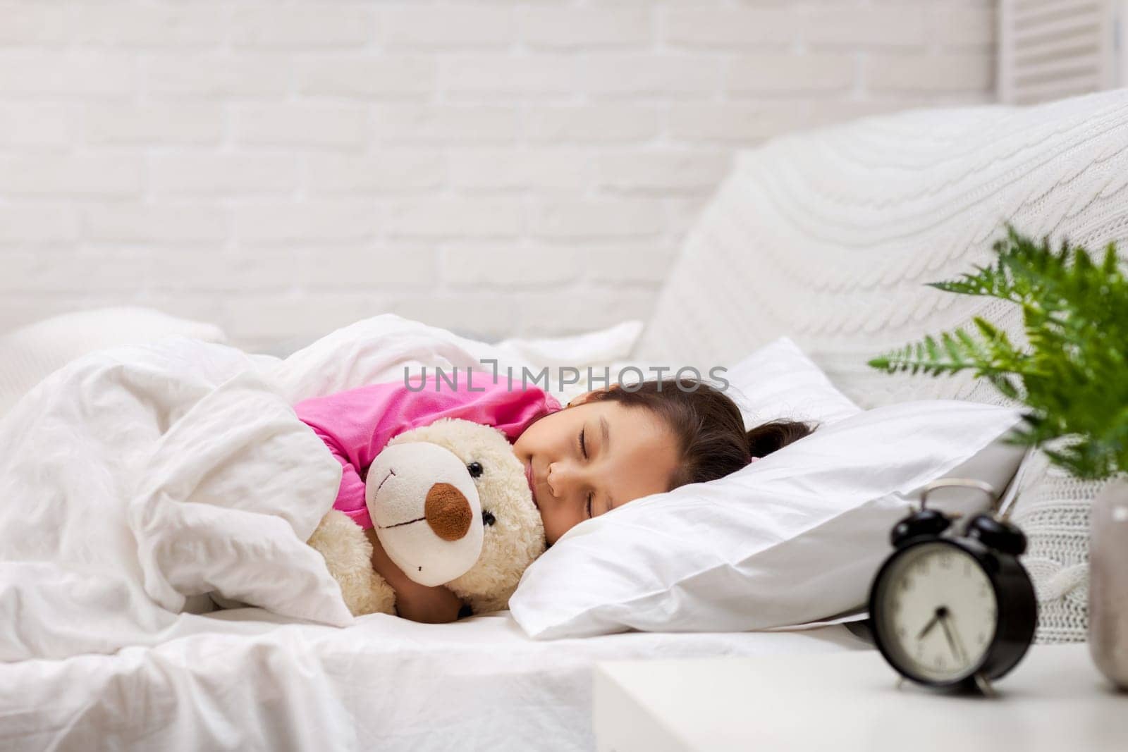 Cute little child girl sleeping with teddy bear in her bed