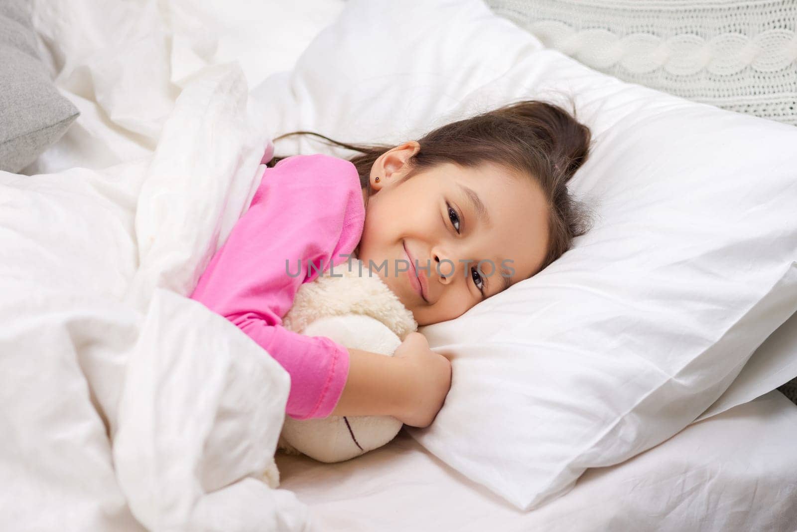 Cute happy little child girl sleeping with teddy bear in her bed