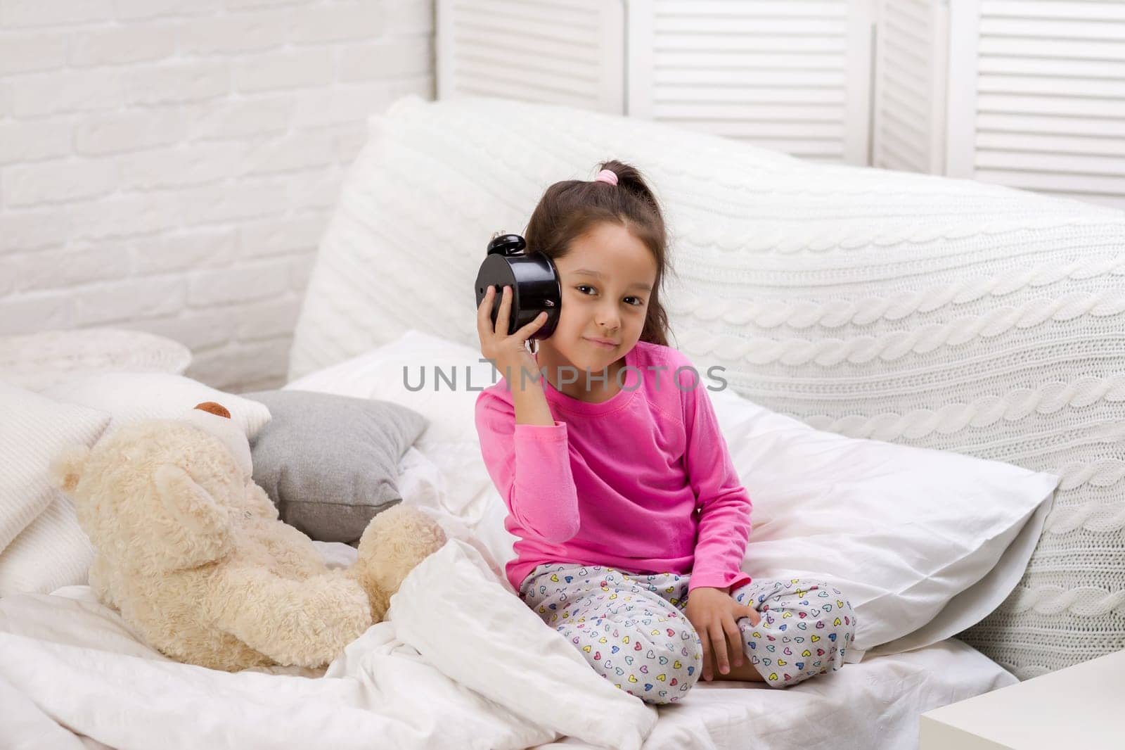 cute little child girl in pyjamas with clock in bed. good morning
