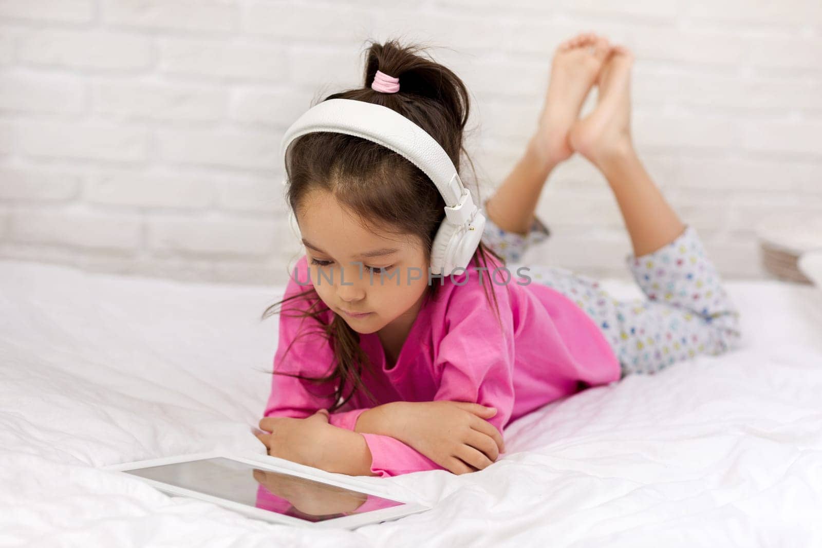 cute little child girl lies in bed uses digital tablet. child playing on tablet pc.