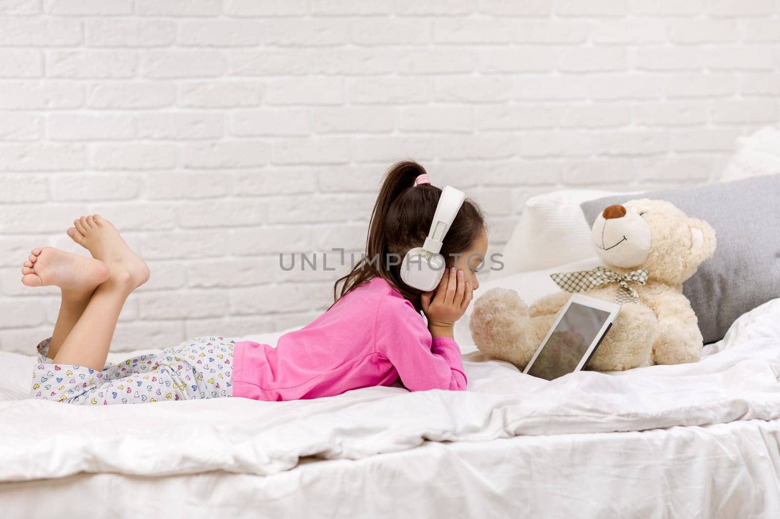 cute little child girl lies in bed uses digital tablet. child playing on tablet pc.