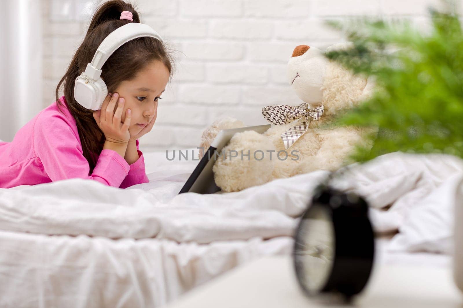 cute little child girl lies in bed uses digital tablet. child playing on tablet pc.