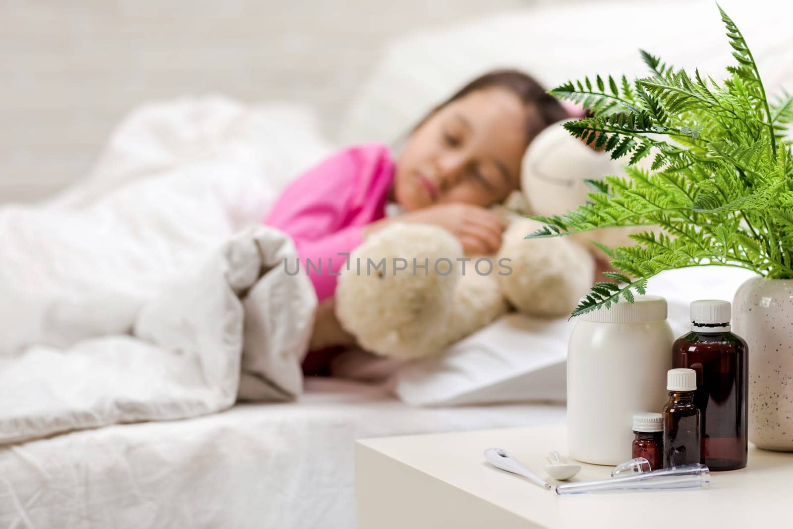 Sick little child girl lying in bed. Cold flu season. focus on medication and pill bottle