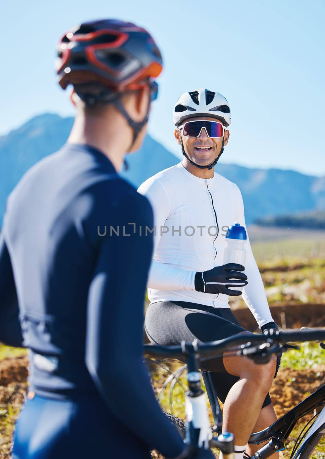 Fitness, bike and friends drinking water in nature, taking a break from their cardio or endurance workout. Exercise, mountain and a man cyclist team in conversation while cycling in the countryside by YuriArcurs