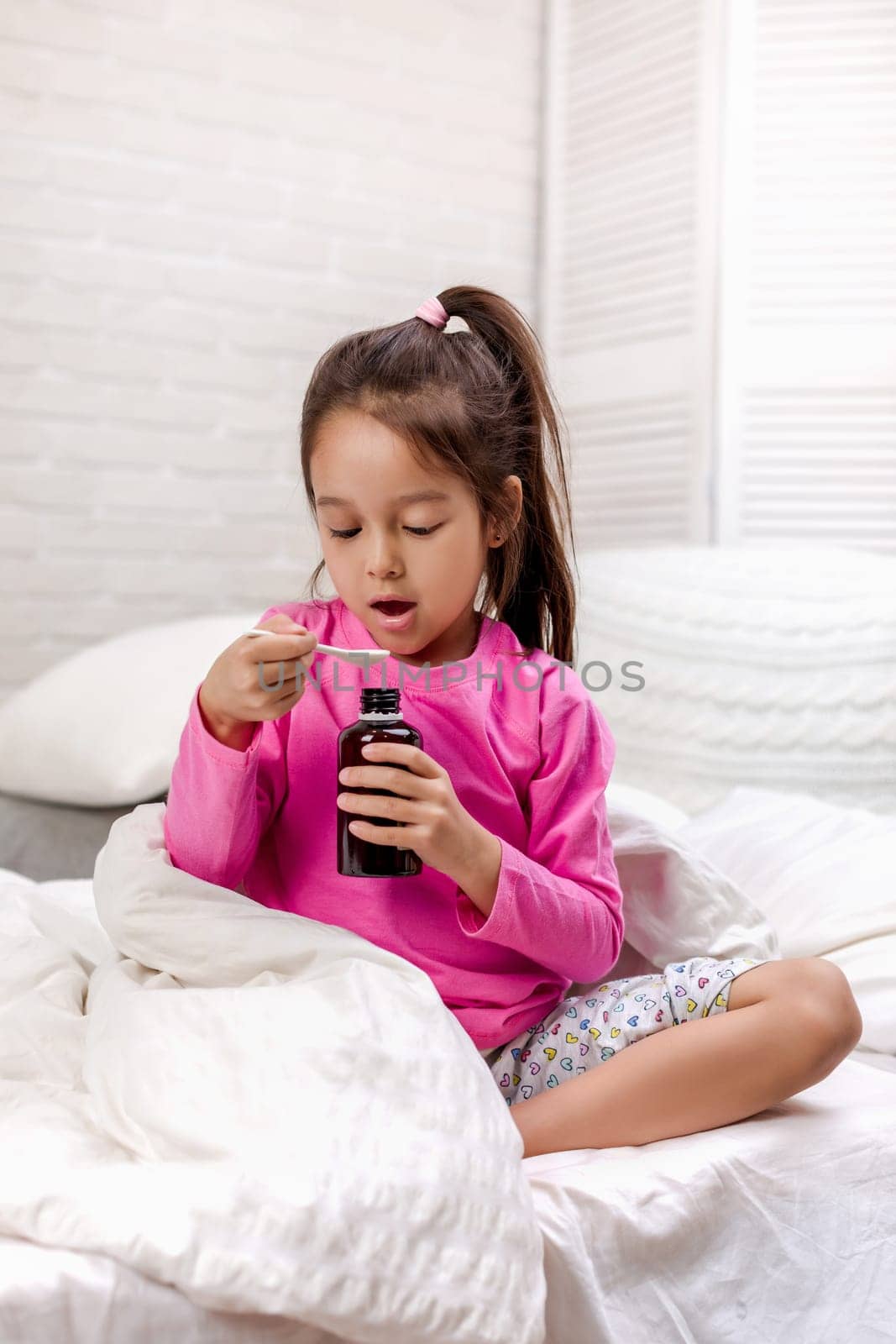 Sick little child girl pouring antipyretic syrup for kid in bed