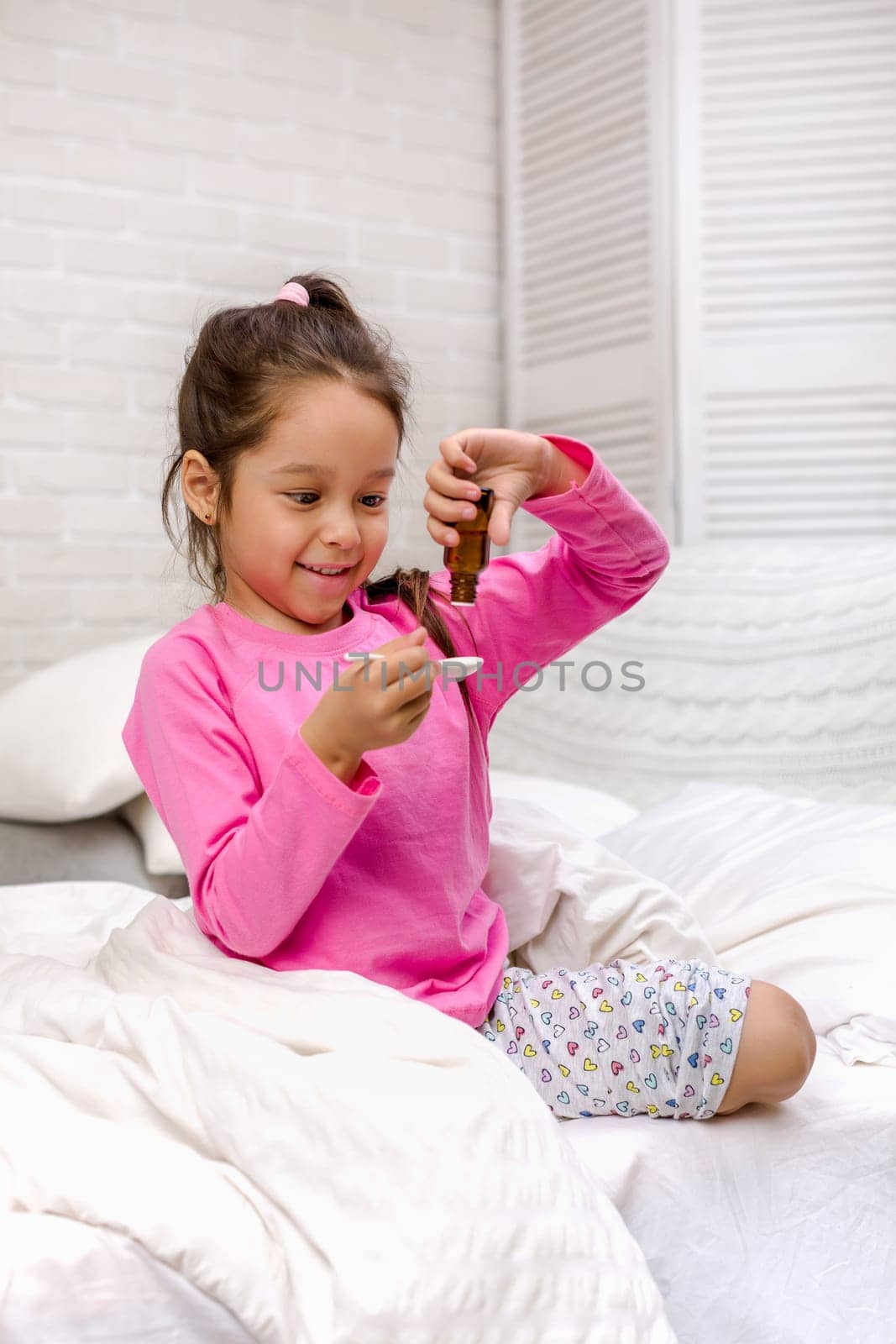 Sick little child girl pouring antipyretic syrup for kid in bed
