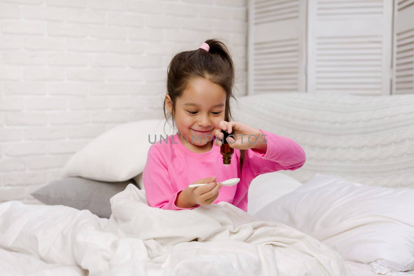 Sick little child girl pouring antipyretic syrup for kid in bed