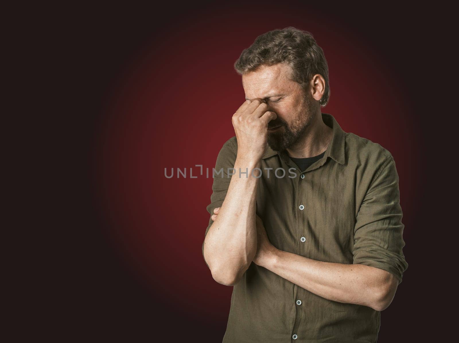 Man facing personal problems and challenges. Mid-aged man with closed eyes, conveying sense of sadness and inner turmoil. Isolated on dark red background, feeling of despair and emotional struggle. by LipikStockMedia
