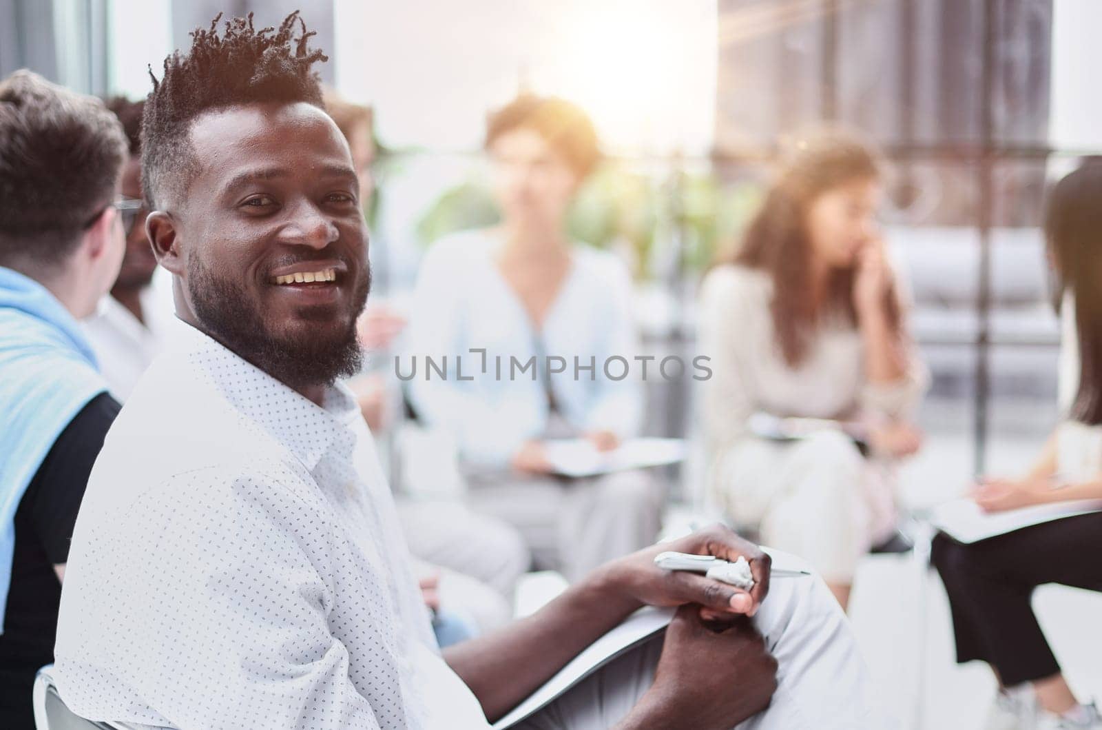 portrait of an African American in a white shirt against the background of his colleagues. looking at the camera