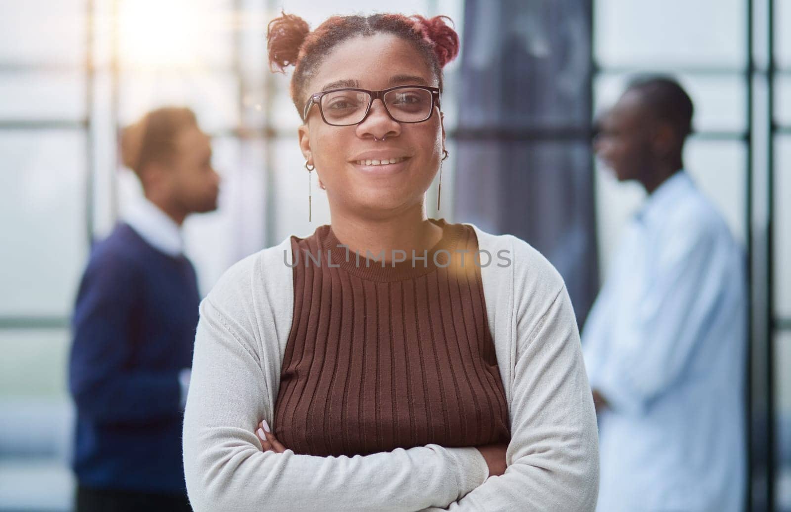 She is standing in a modern office with her colleagues in the background.