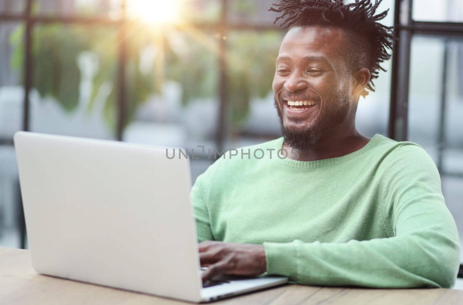 Young african american business man sitting in loft office or cafe, working on new online IT startup project, using laptop by Prosto