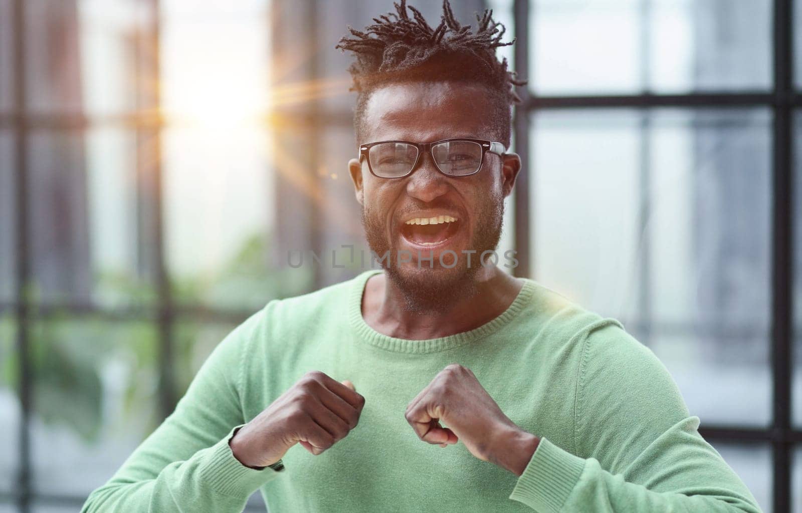 Winning ecstatic young African man clenching his fists with excited face