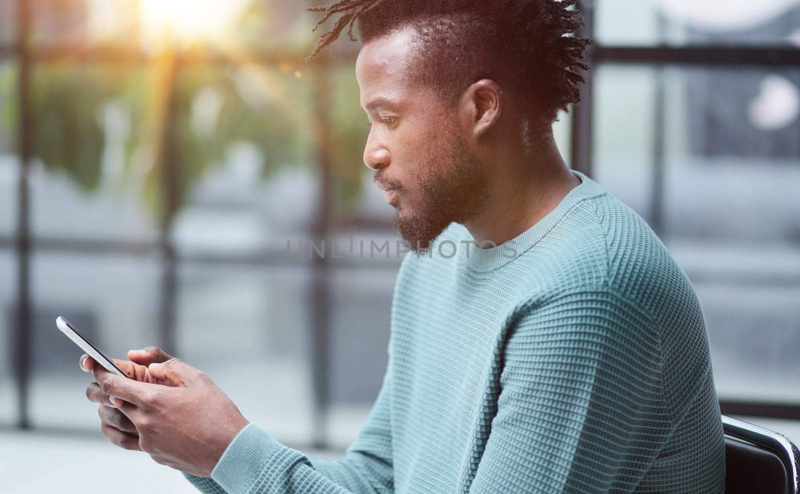 Black man looking at smartphone browsing internet, office technology and digital communication
