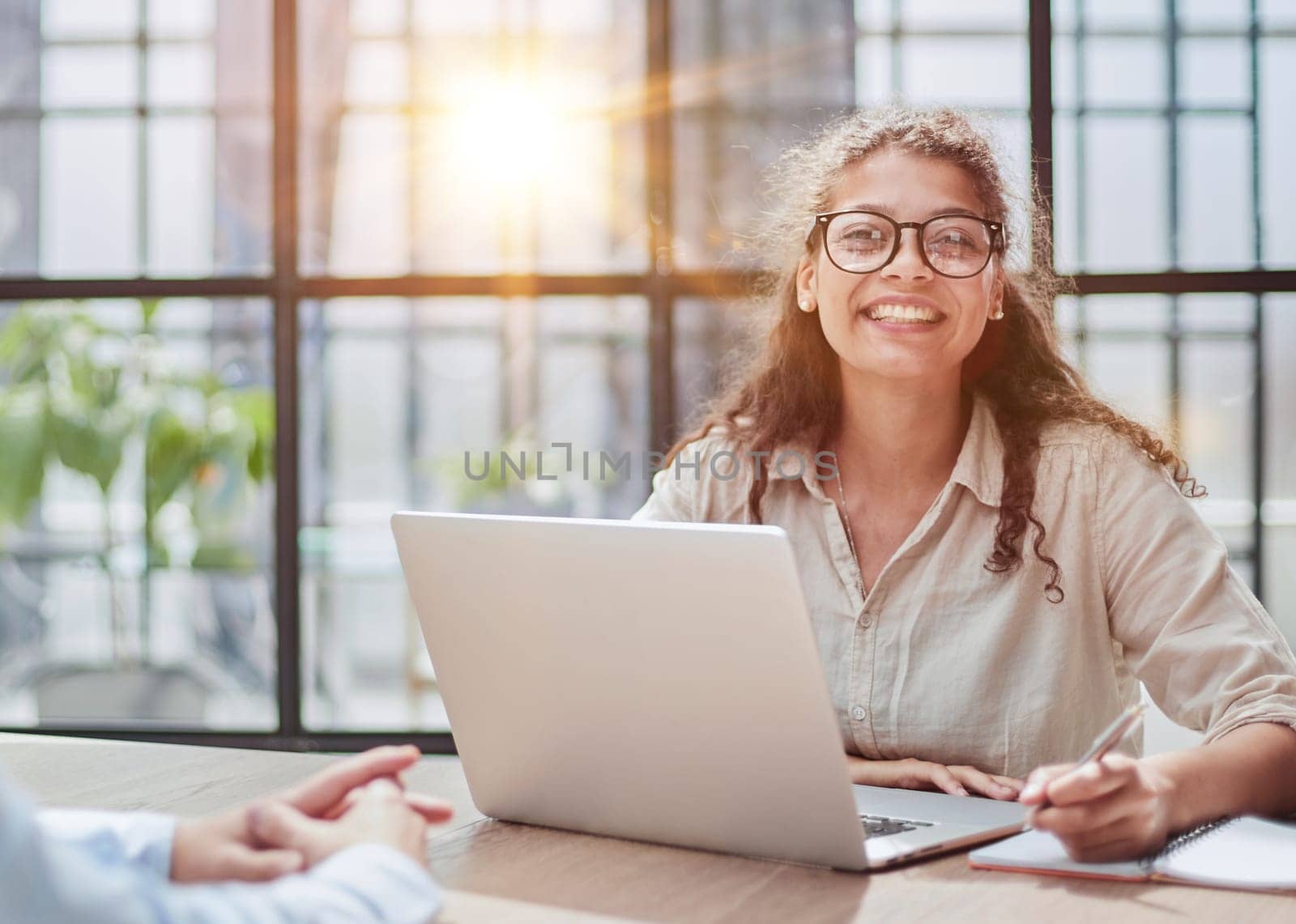 manager in glasses sitting at the table receives a client in the office looking at the camera