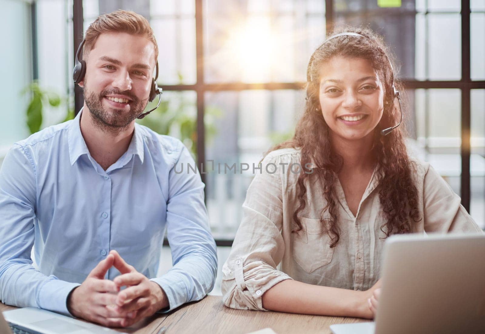 smilling man and charming woman are sitting at laptops in headphones by Prosto