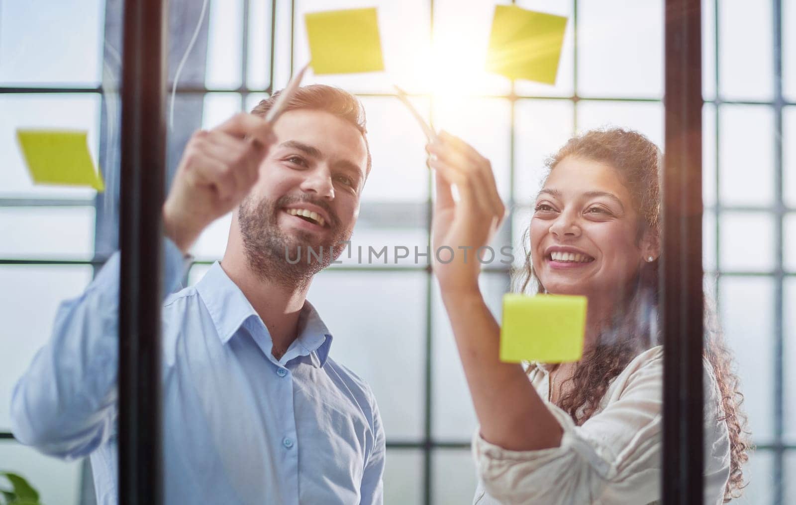 Creative professionals standing and discussing in office behind glass wall with sticky notes