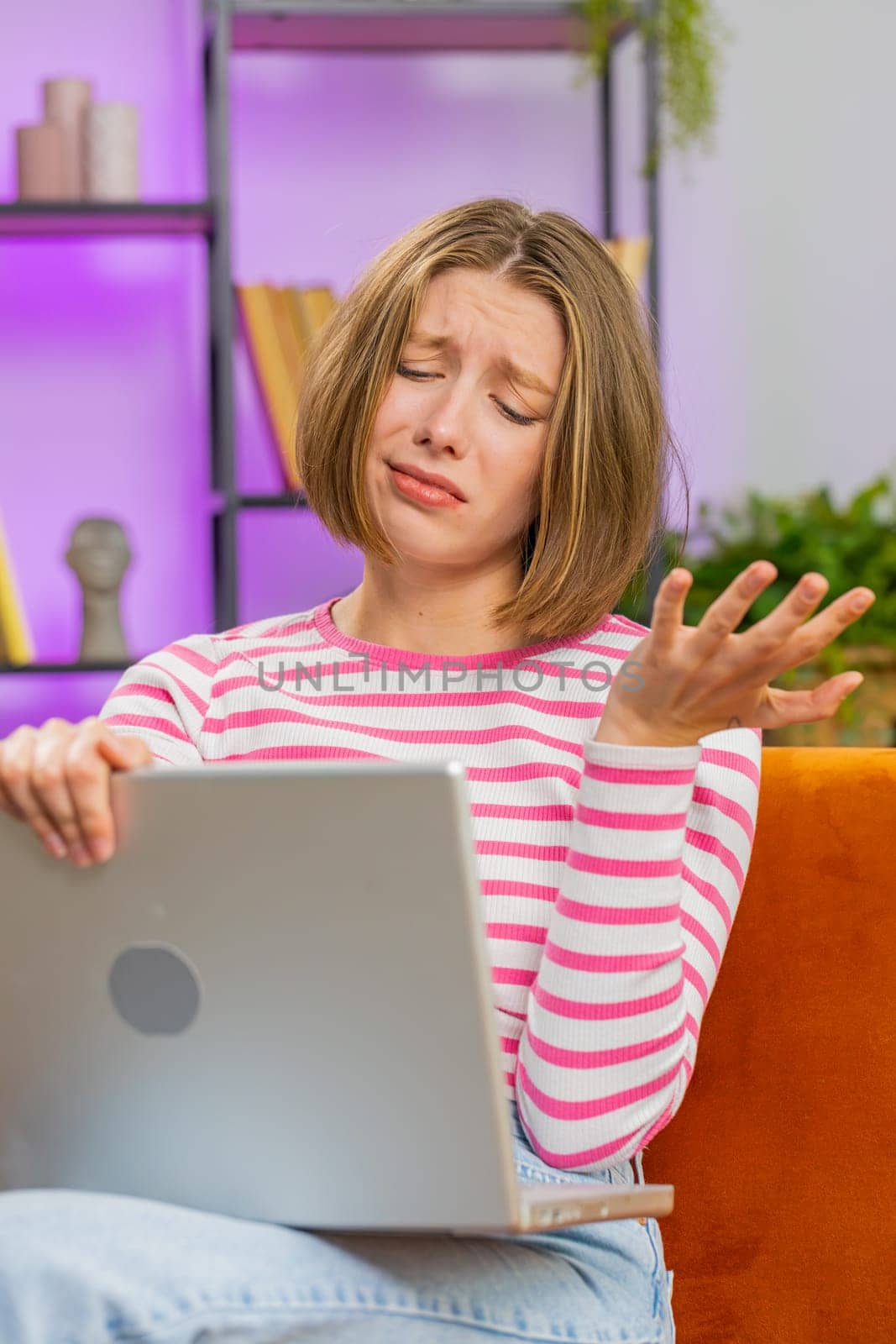 Displeased young woman use laptop notebook typing browsing working, loses becoming surprised sudden lottery results bad news fortune loss fail computer virus. Girl at home in room on couch. Vertical