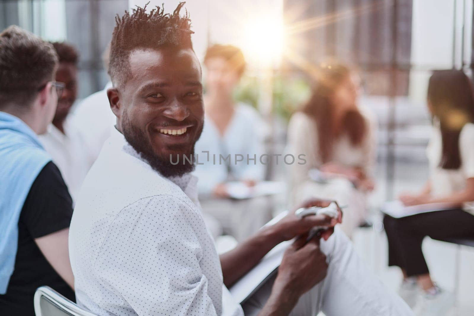 portrait of an African American in a white shirt against the background of his colleagues. looking at the camera