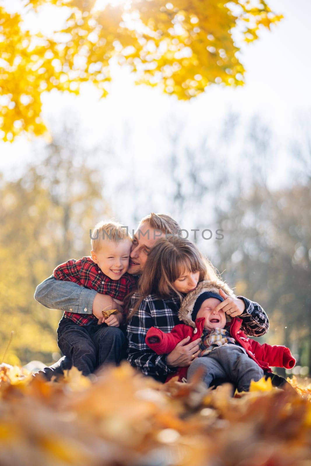 A young family sits in the park on a leafy, sunny autumn day