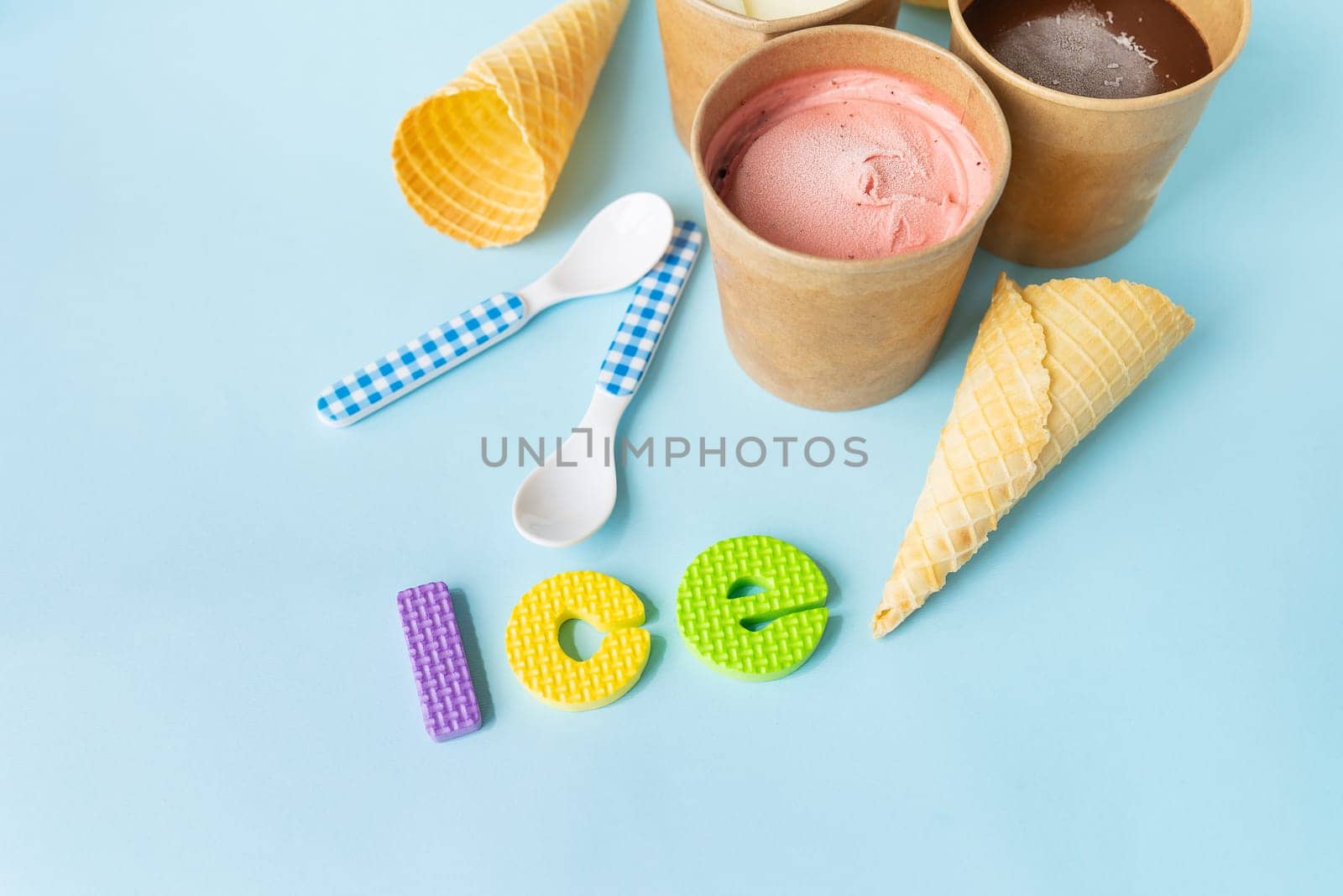 Ice cream in a box with different flavors - strawberry, chocolate, vanilla stands on a blue background along with a waffle cone and a spoon. Ice inscription