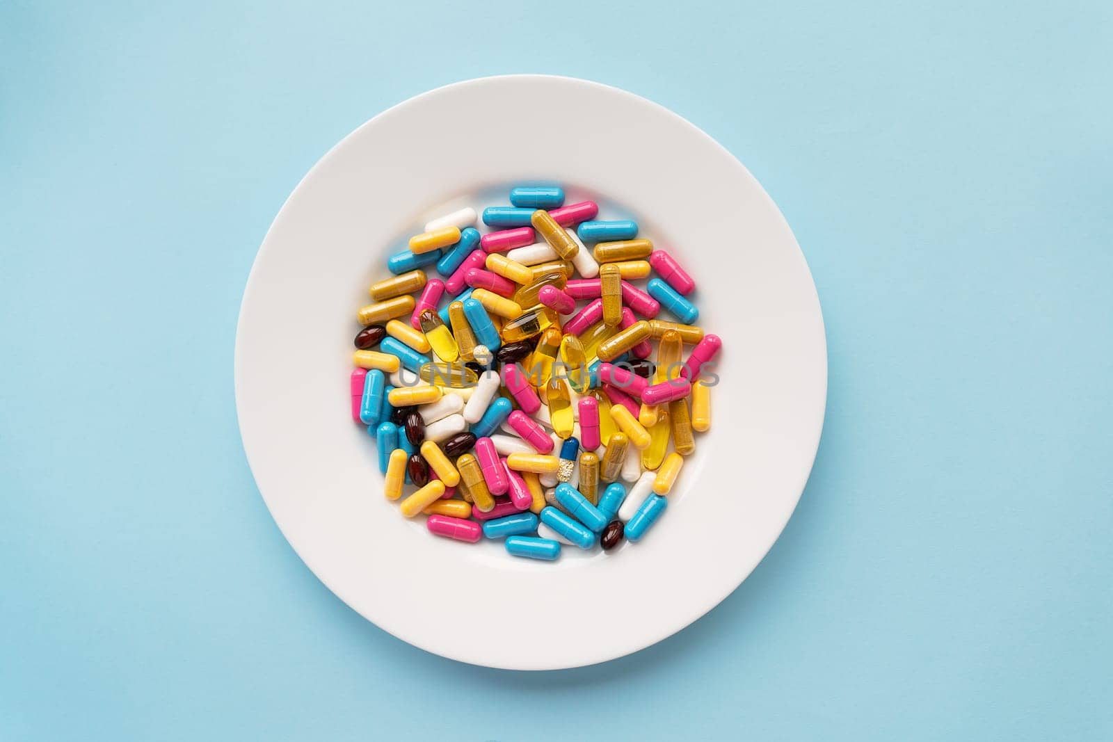 Colorful pills in a large white bowl on a blue background. The concept of health and evidence-based medicine. Place for an inscription