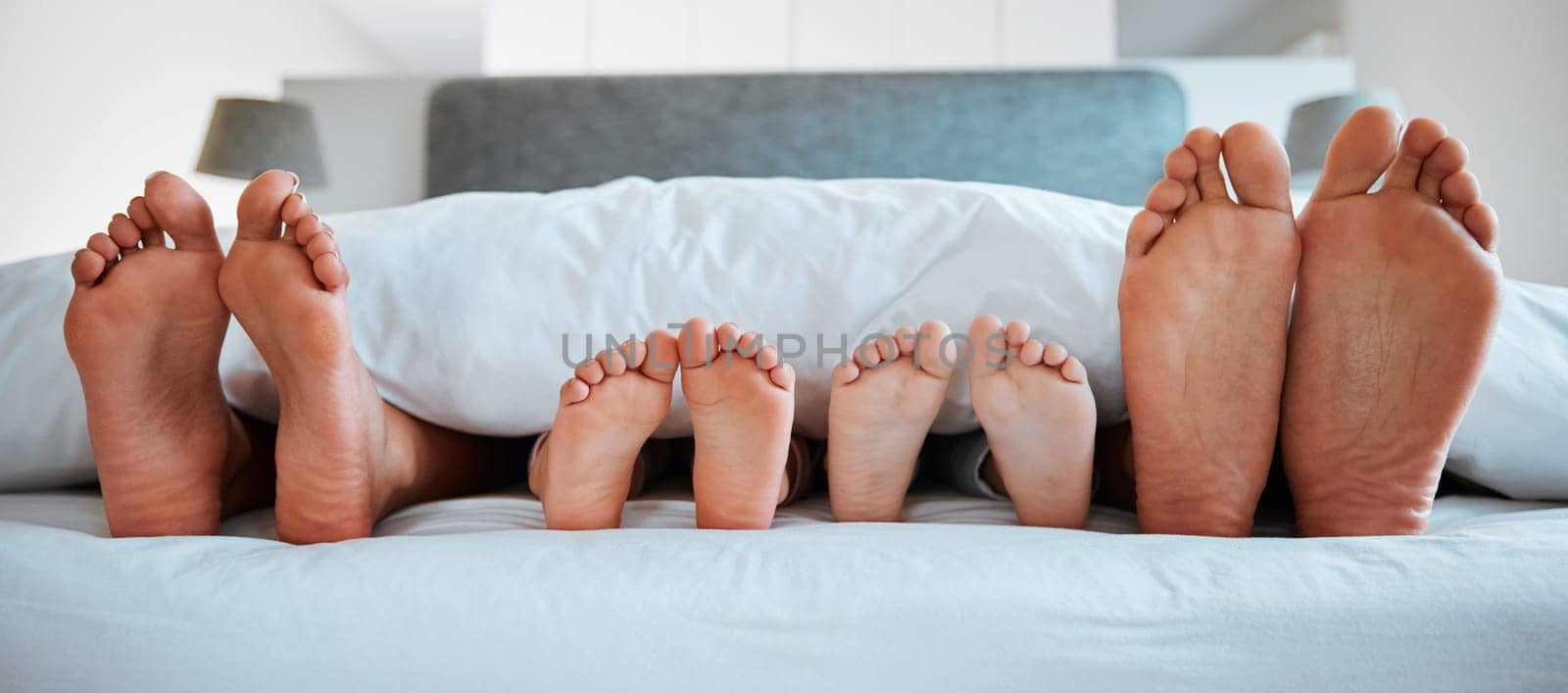 Family feet, bed and blanket in closeup, parents or kids sleeping on holiday in morning, care and relax. Bedroom, people and sleep with mom, dad or children on vacation, home or break in hospitality.
