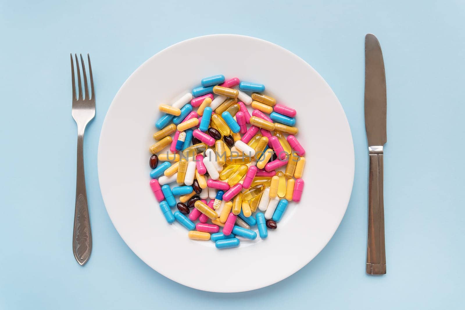 Many multi-colored bright vitamins lie on a plate along with a knife and fork. The concept of healthcare, healthy eating, diet
