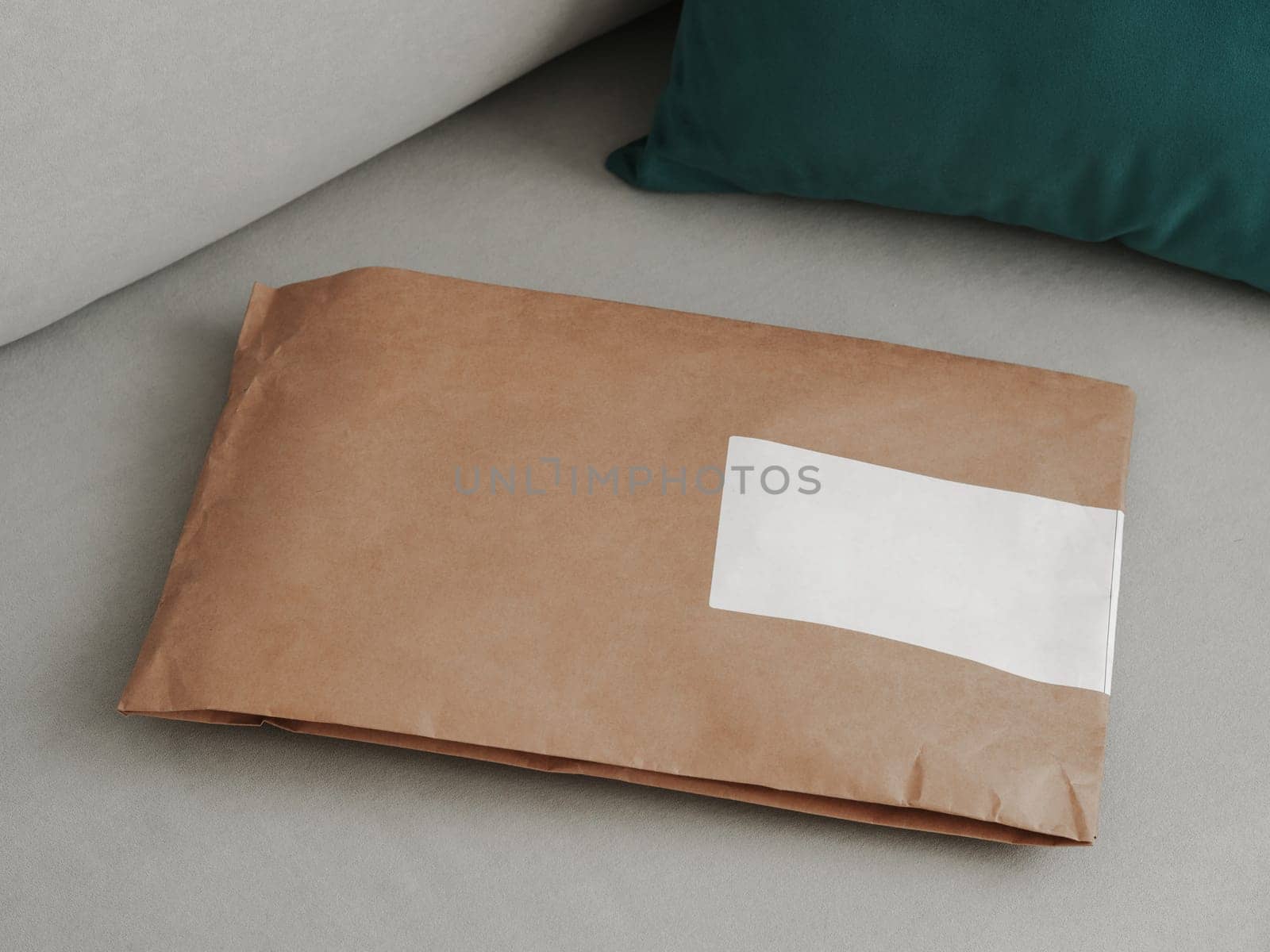Craft paper soft pack on gray scandinavian sofa background with blank space. Shopping, Delivery, shipping, Package concept. Closed soft package on sofa in modern interior of home.