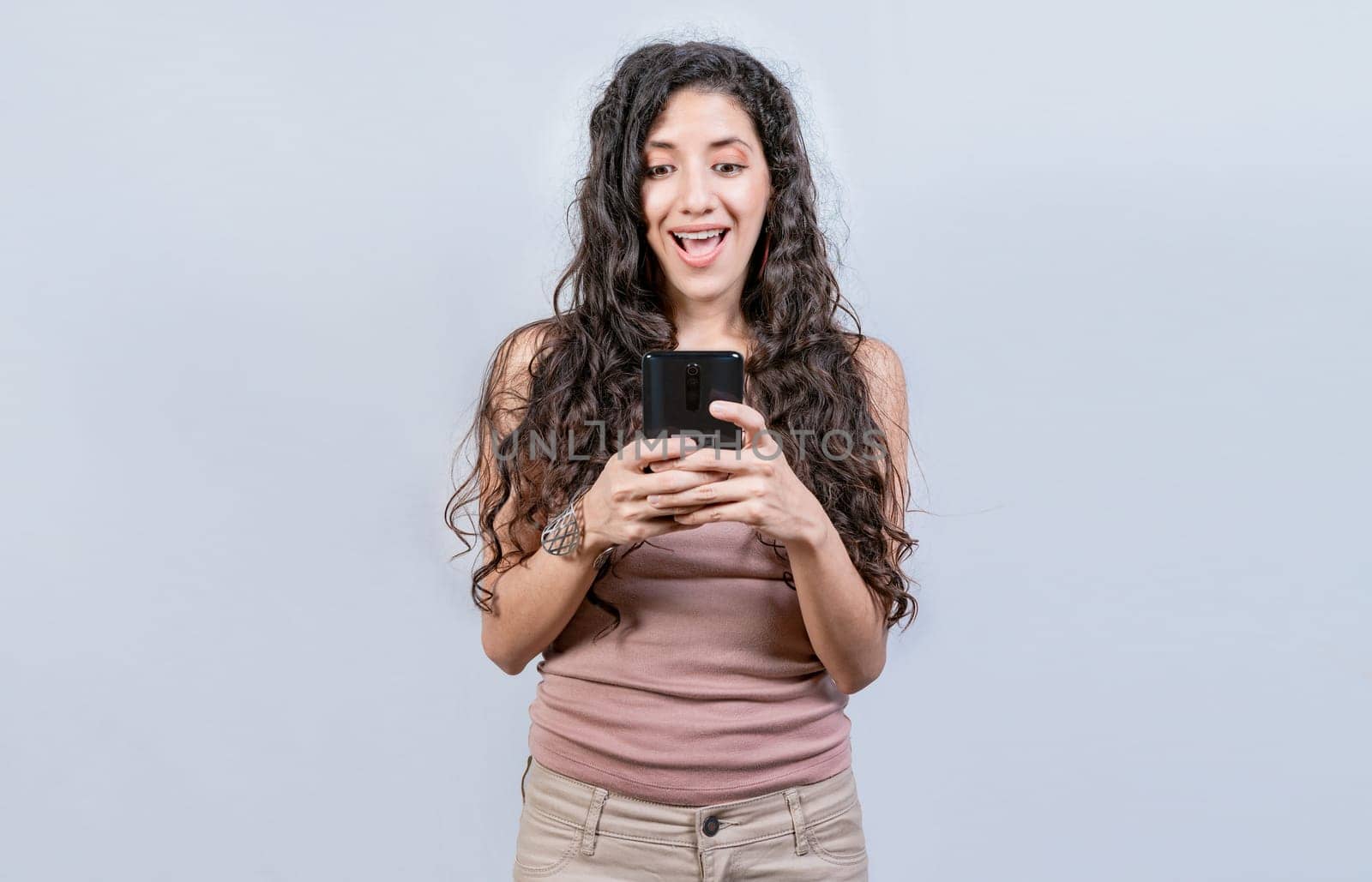 Happy and surprised girl looking at a promotion on the cell phone. Smiling woman texting with cell phone isolated. Happy latin girl using cell phone isolated by isaiphoto