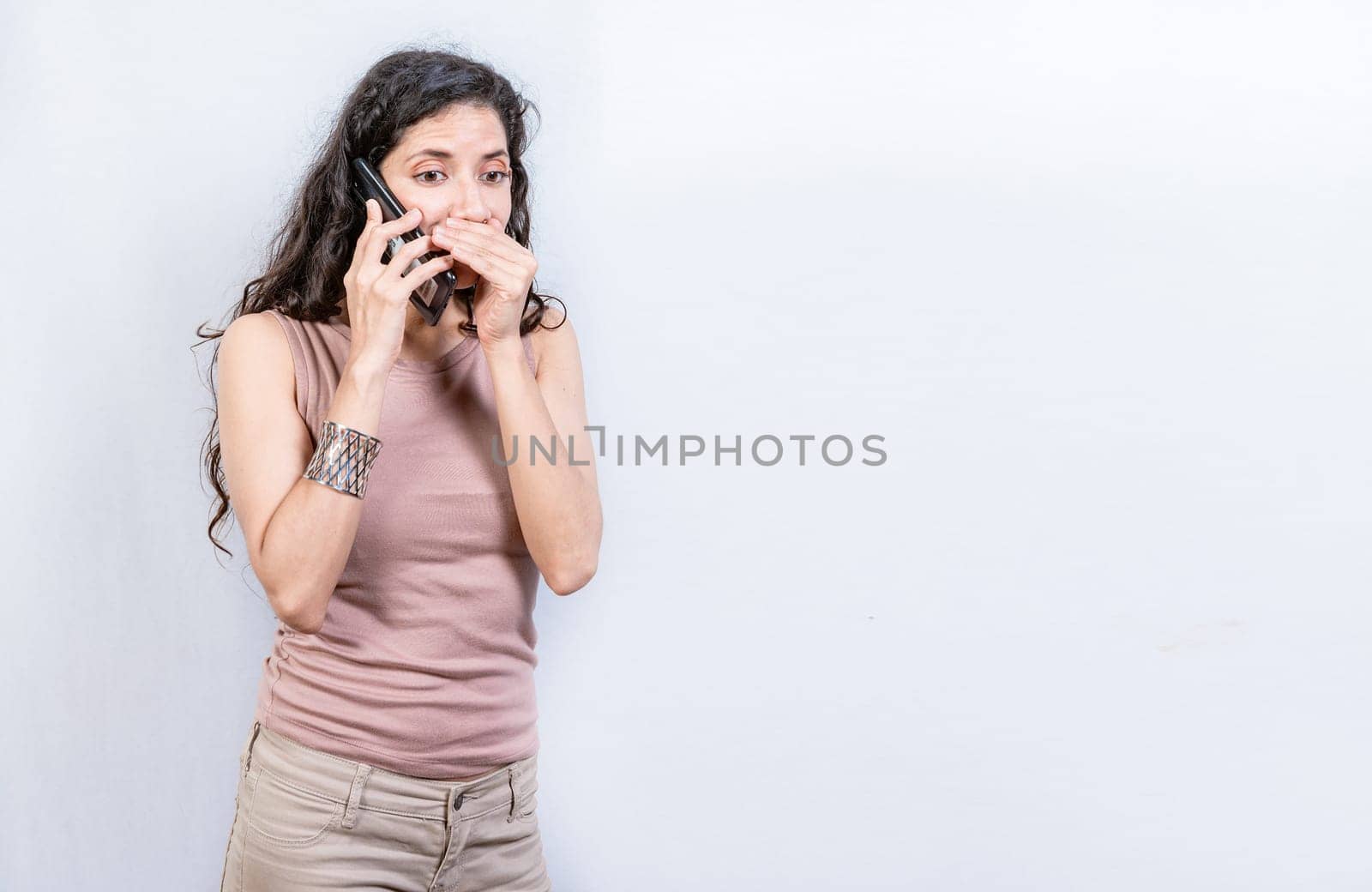 Mysterious young woman talking on the phone isolated. Woman talking secretly on the phone isolated. Latin woman talking on the phone quietly isolated.