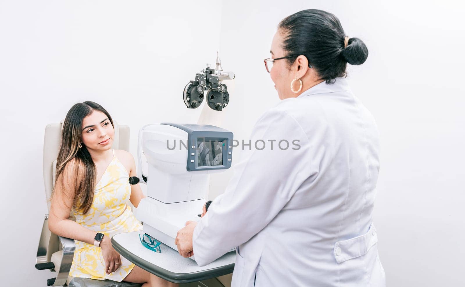 Optometrist with female patient in the autorefractor. Woman patient having consultation with optometrist in office by isaiphoto