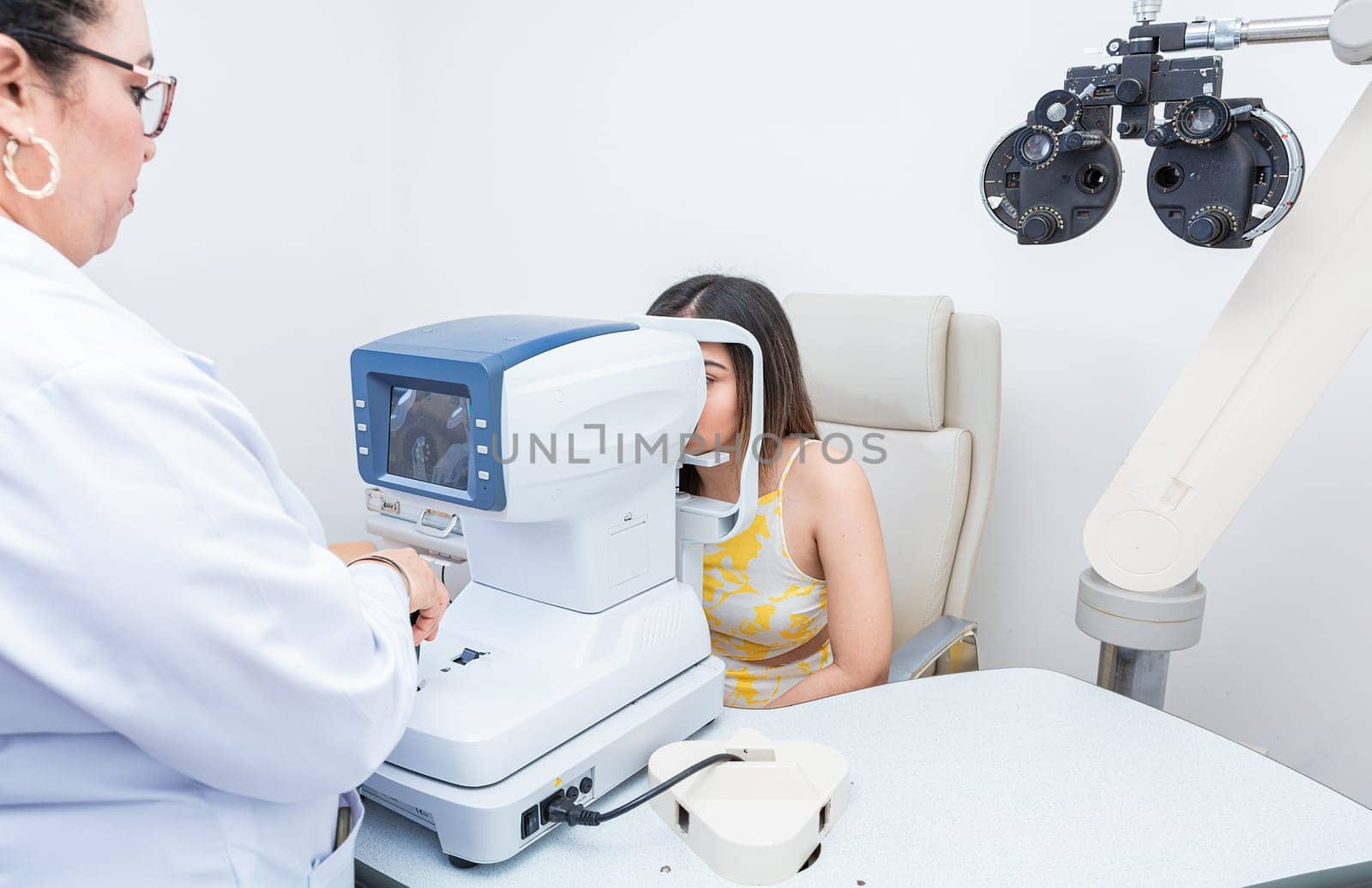 Specialist performing eye exam to female patient. Optometrist checking the eyesight of a patient with an autorefractor by isaiphoto