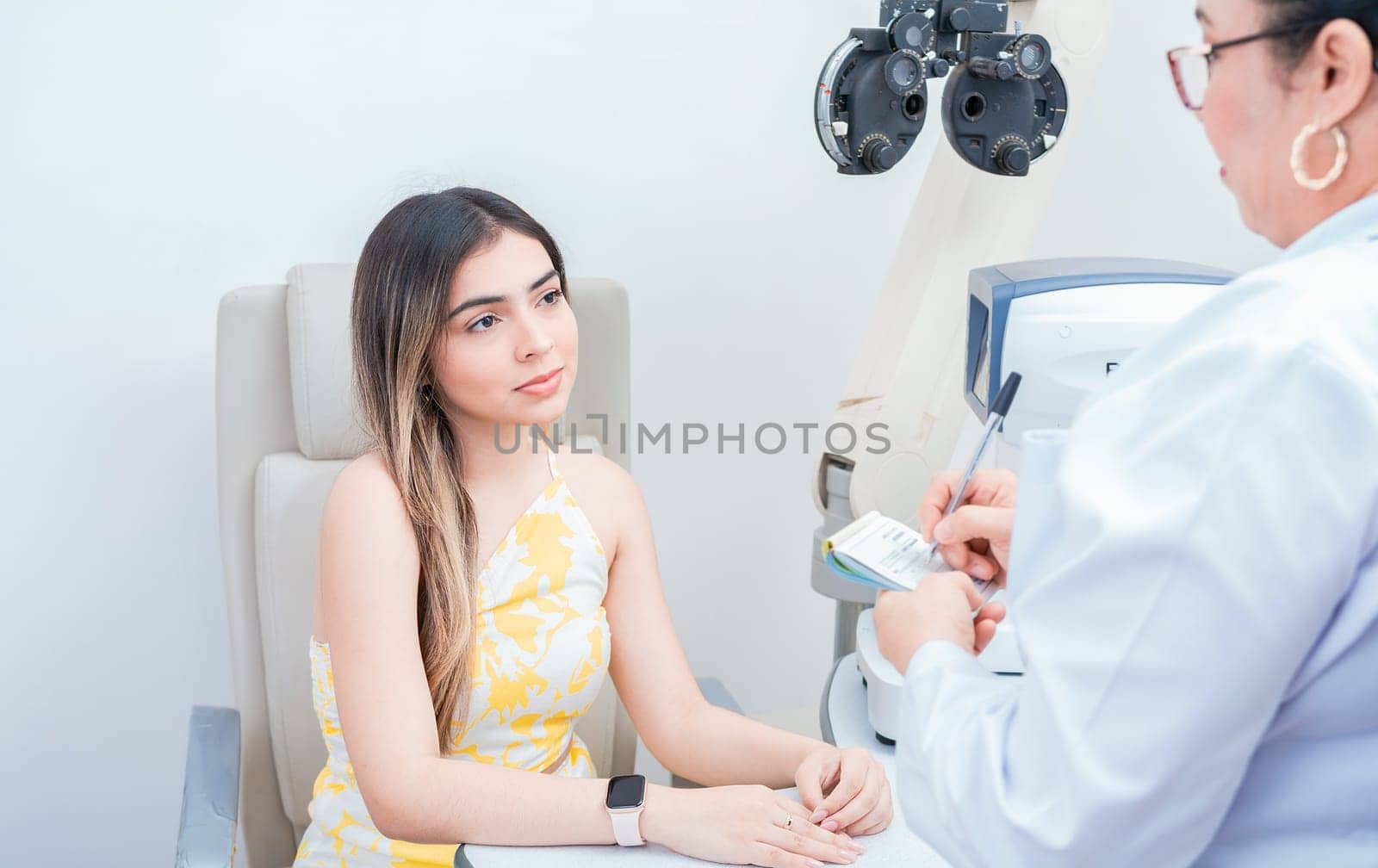 Female patient having consultation with optometrist in office. Optometrist with female patient taking notes in office.