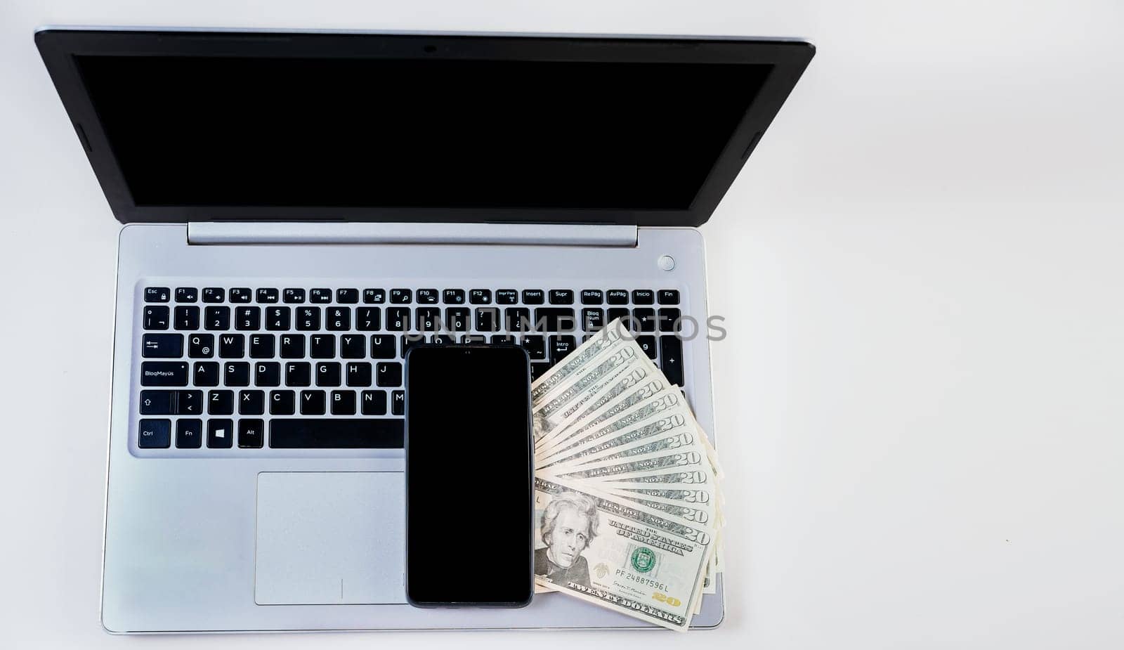 Top view of laptop with cell phone and dollar bills. Cell phone on laptop keyboard and dollar bills. Mobile phone on top of dollar bills on laptop keyboard by isaiphoto