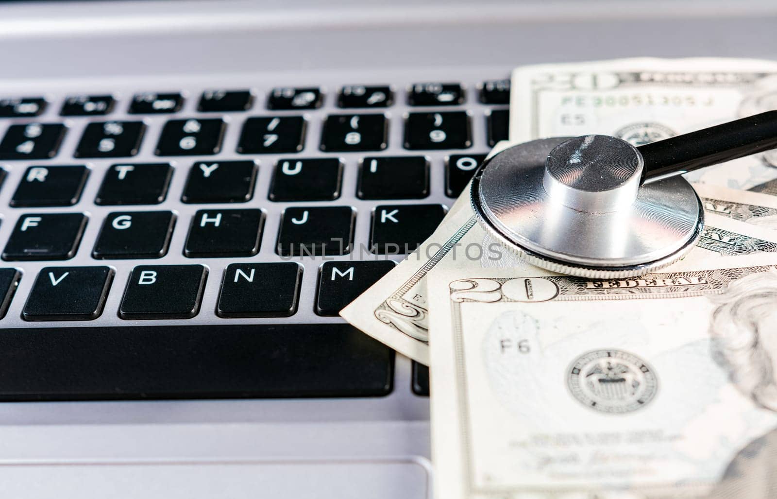 Stethoscope on dollar bills on top of laptop keyboard. Stethoscope on top of money on laptop keyboard