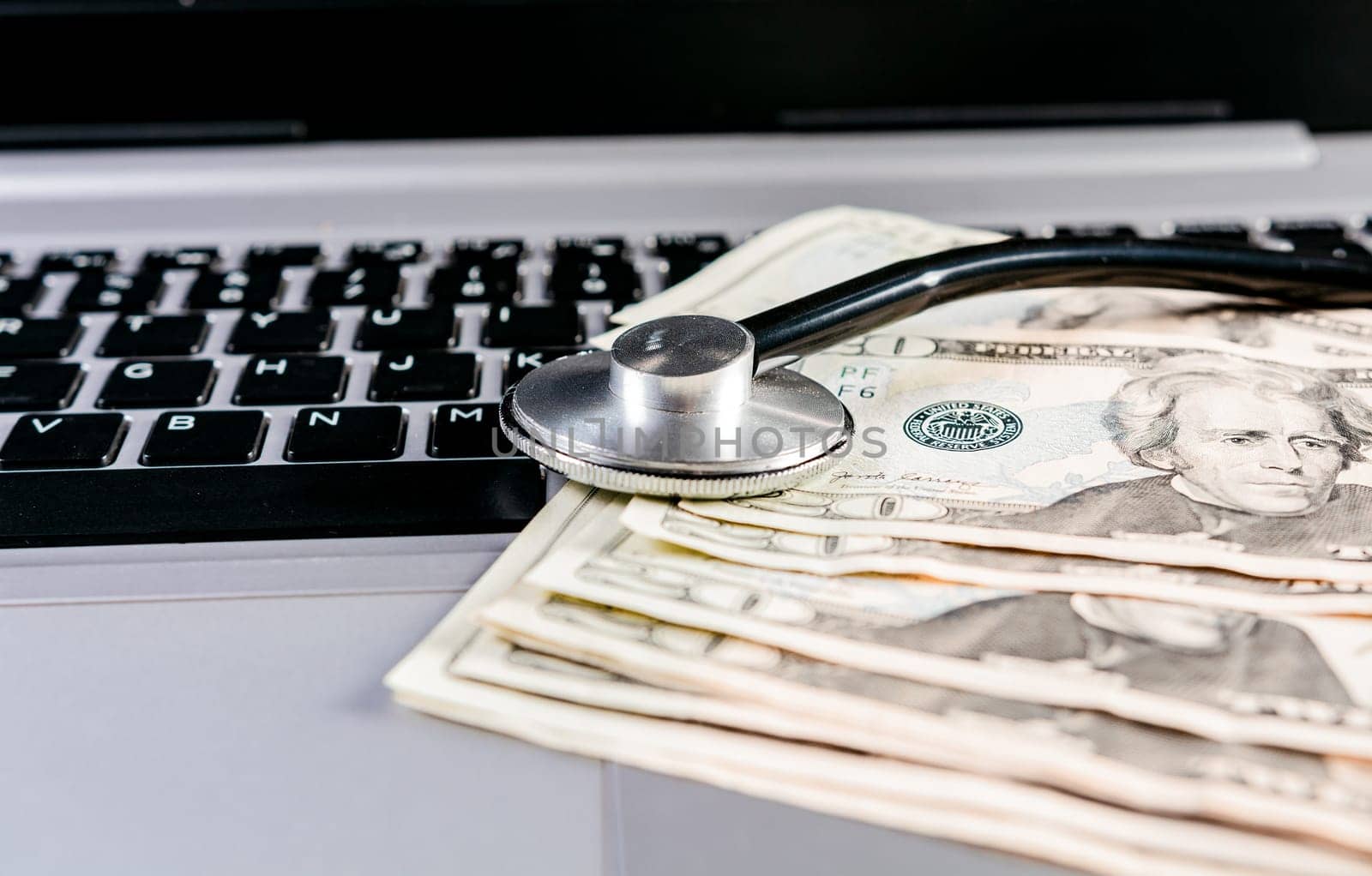 Stethoscope on top of money on laptop keyboard. Stethoscope on dollar bills on top of laptop keyboard by isaiphoto