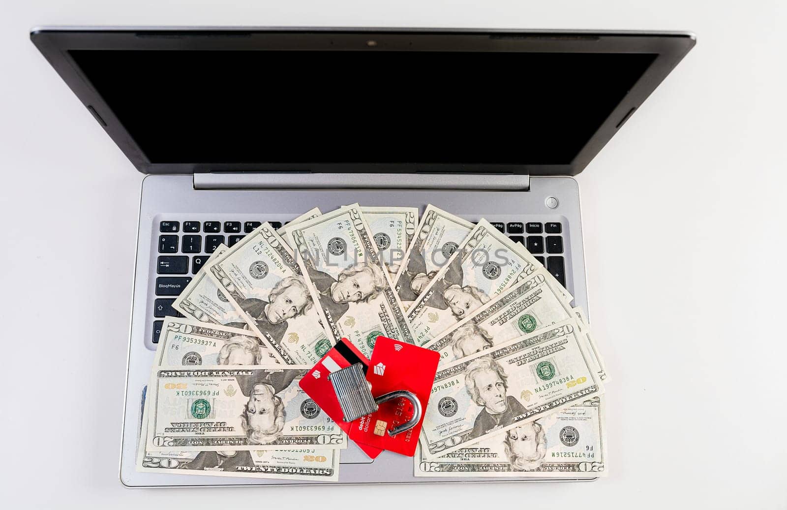 Top view of padlock with credit card on top of dollars on laptop keyboard. Padlock on top of credit card over dollar bills on computer keyboard by isaiphoto