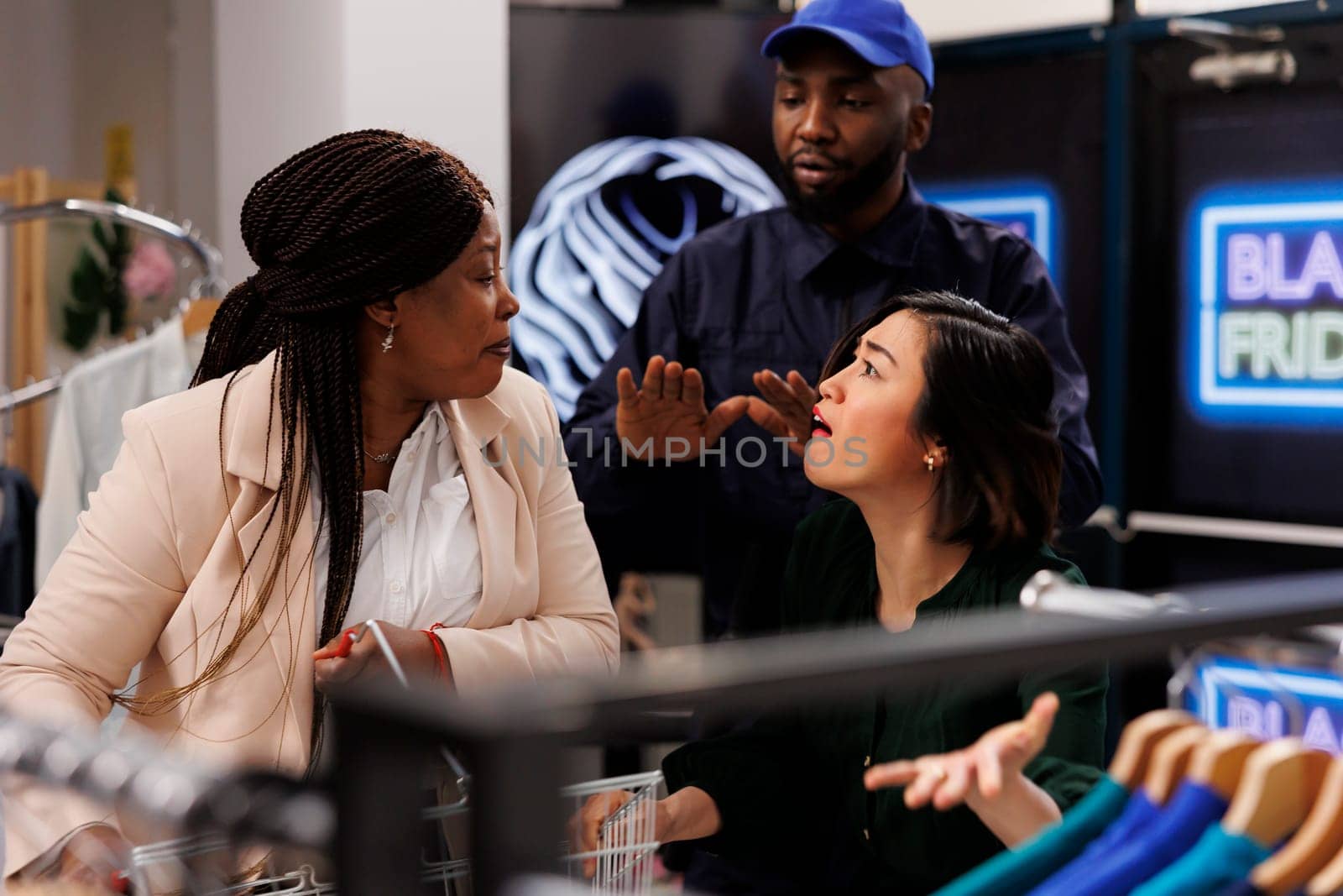 Two diverse women fighting over discount items during Black Friday shopping. Security guard dealing with crazy bargain hunters in clothing store, people going crazy with seasonal sales