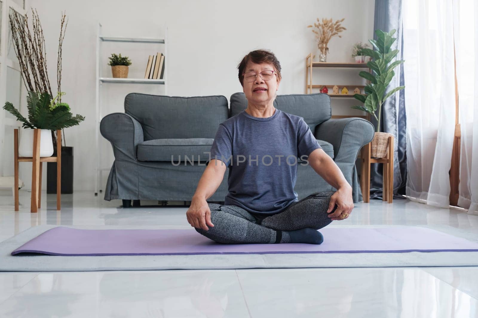 A senior woman finds inner peace through yoga and meditation at home, embracing relaxation and tranquility of the mind. Calm barefoot middle aged female sitting on carpet in half lotus posture, making mudra gesture and closing eyes, having peaceful facial expression, doing mindful meditation, concentrating on breathing.