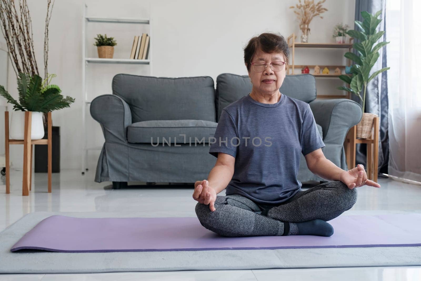 A senior woman finds inner peace through yoga and meditation at home, embracing relaxation and tranquility of the mind. Calm barefoot middle aged female sitting on carpet in half lotus posture, making mudra gesture and closing eyes, having peaceful facial expression, doing mindful meditation, concentrating on breathing.