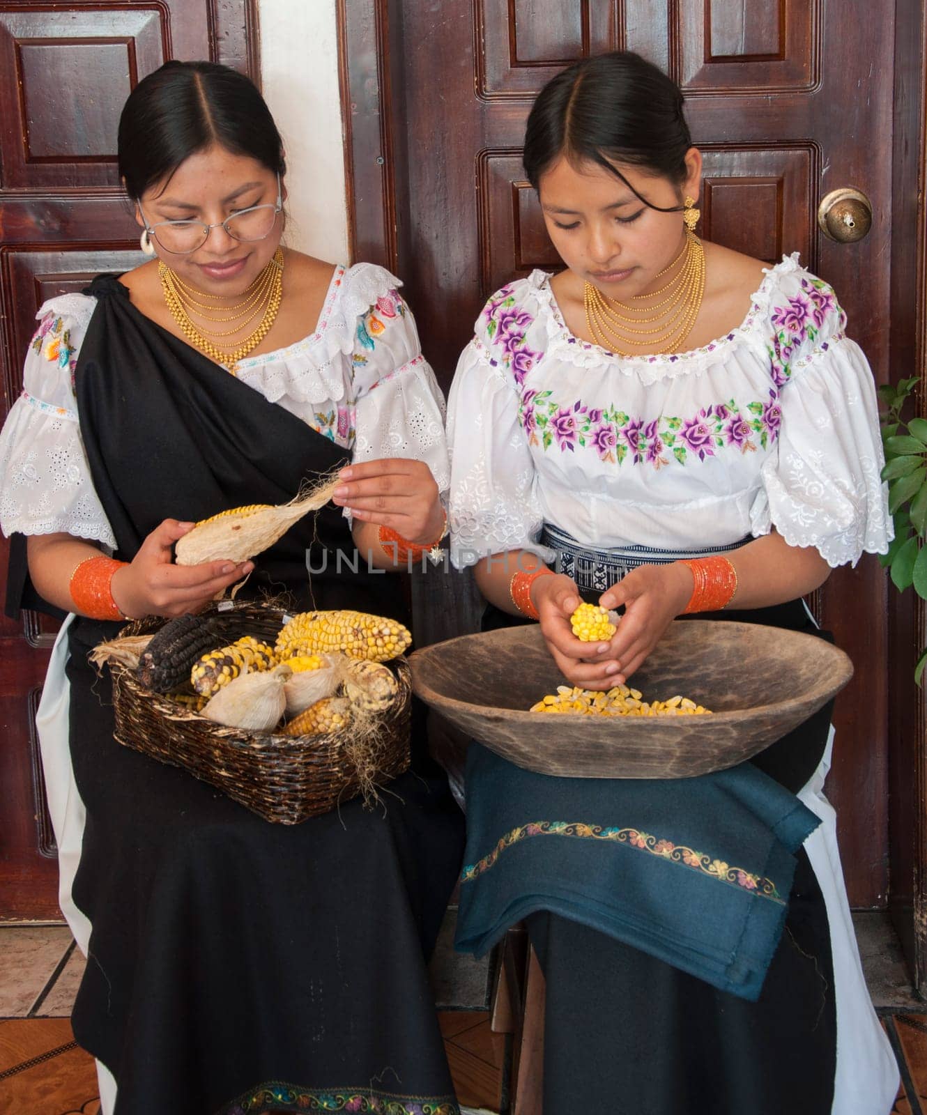 two indigenous women in traditional dresses in a house shelling ears of corn. High quality photo